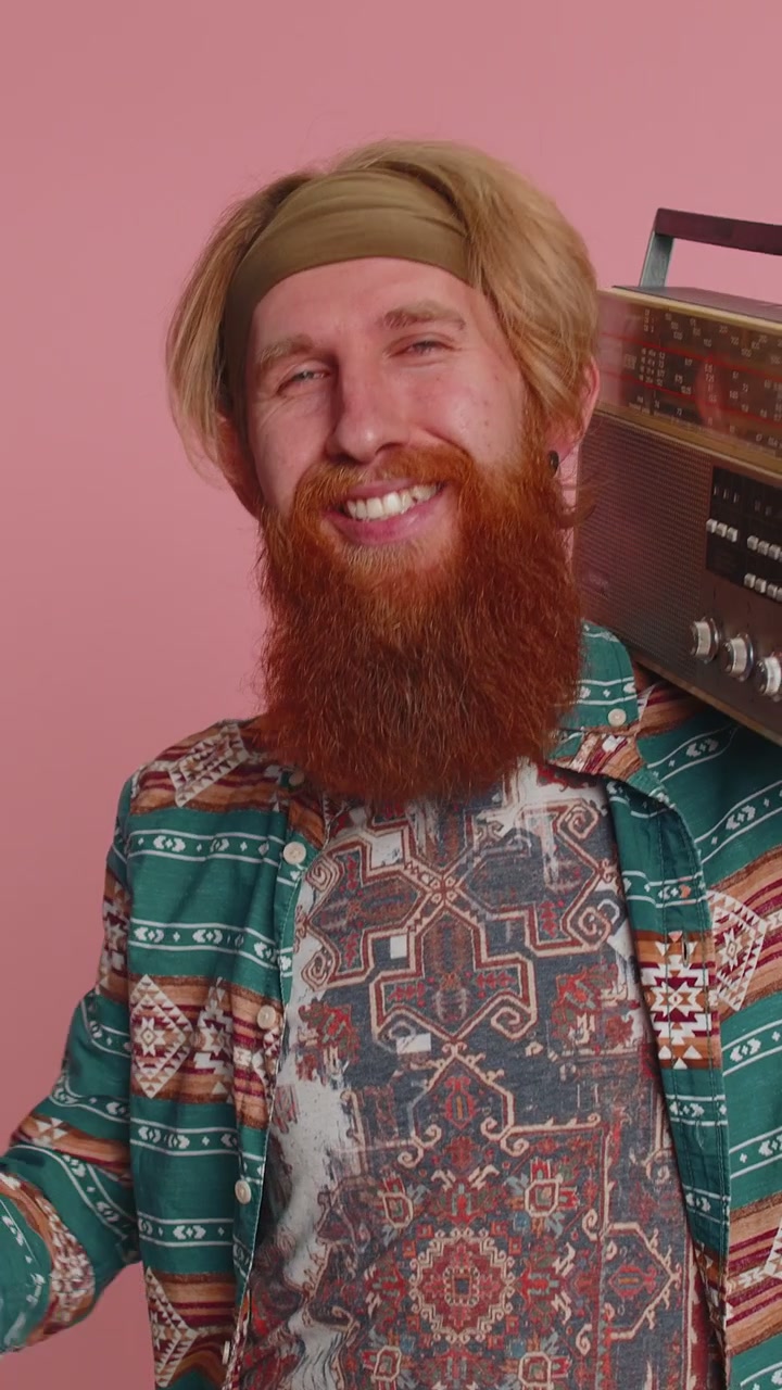 Punatukkainen hippimies käyttää retro-kasettisoitinta kuunnellakseen musiikkia, diskoilee ja pitää hauskaa.