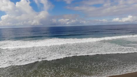 Eine-Drohne-Dreht-Und-Windet-Sich-über-Tosenden-Wellen-Und-Enthüllt-Surfer,-Die-Am-Strand-Surfen