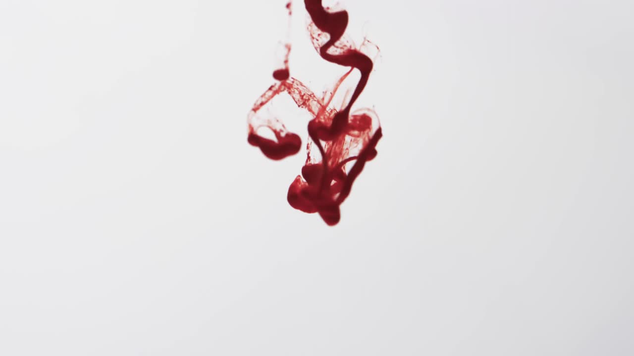 video en cámara lenta de tinta de acuarela roja mezclándose en agua contra un fondo gris