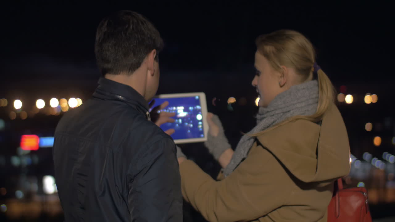 una pareja tomando fotos de la ciudad nocturna con una tableta.