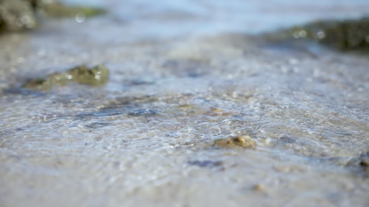 바다의 파도는 산란한 바위와 함께 모래 해변을 부드럽게 습니다.