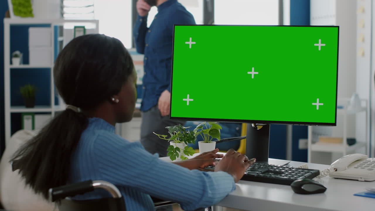 Sort lammet forretningskvinde, der sidder i kørestol og bruger pc med grøn skærm