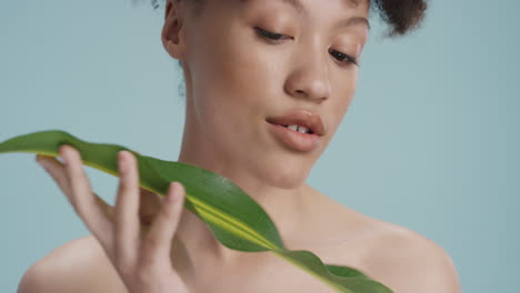 close up portrait attractive young woman touching leaf caressing smooth healthy skin complexion enjoying playful natural beauty on blue background skincare concept