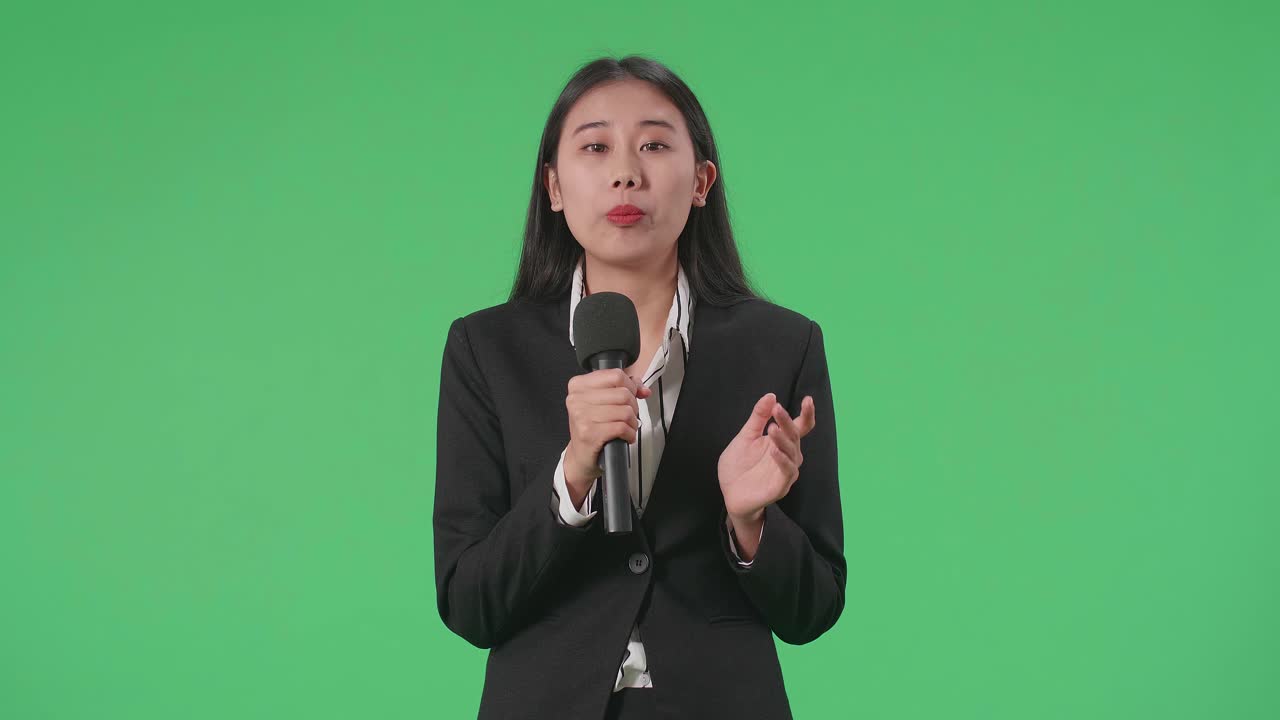 アジアの女性ジャーナリストがグリーンスクリーンでマイクに話します
