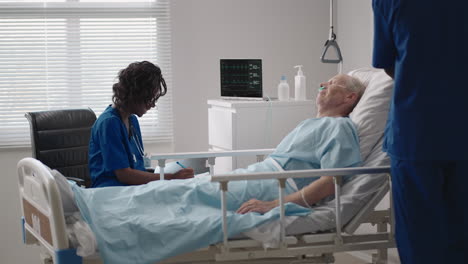 caring african ethnic medical team at the bedside of an elderly male patient. caring health care providers monitor vital signs of an elderly male hospital patient