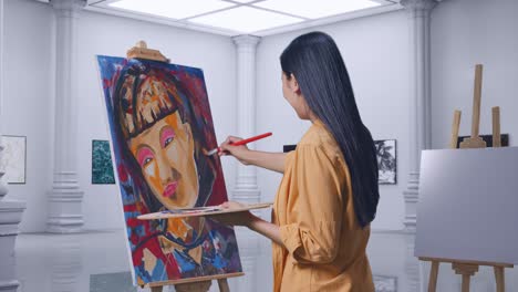 side view of asian female artist crossing her arms and looking at picture while painting a girl on the canvas by oil paints and brush in gallery