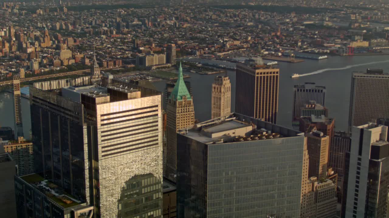 Veduta dall'alto di Wall Street e degli edifici circostanti a New York City mentre una barca si muove lungo l'East River e lo skyline di Brooklyn riempie lo sfondo - ripresa a mano libera.
