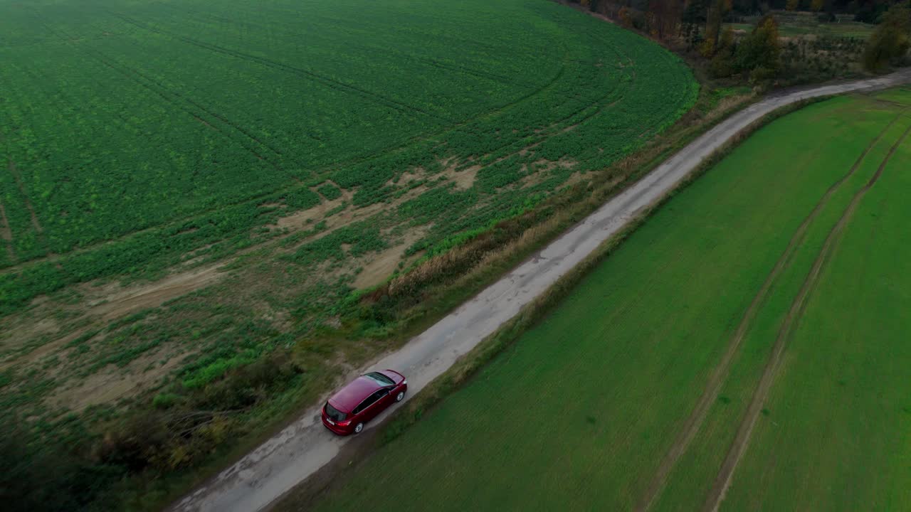un dron aéreo se disparó hacia adelante sobre un camión rojo que conducía por una carretera entre campos agrícolas a lo largo de un campo verde durante el día