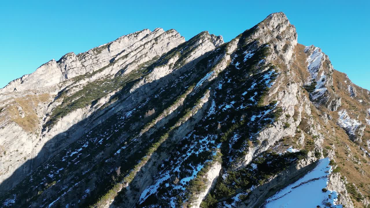 Filmato aereo realizzato con drone sopra Cluat, Italia: vette alpine spettacolari con un forte contrasto tra pendii illuminati dal sole e aree ombreggiate coperte di neve. Ideale per progetti invernali, di montagna e naturalistici cinematografici