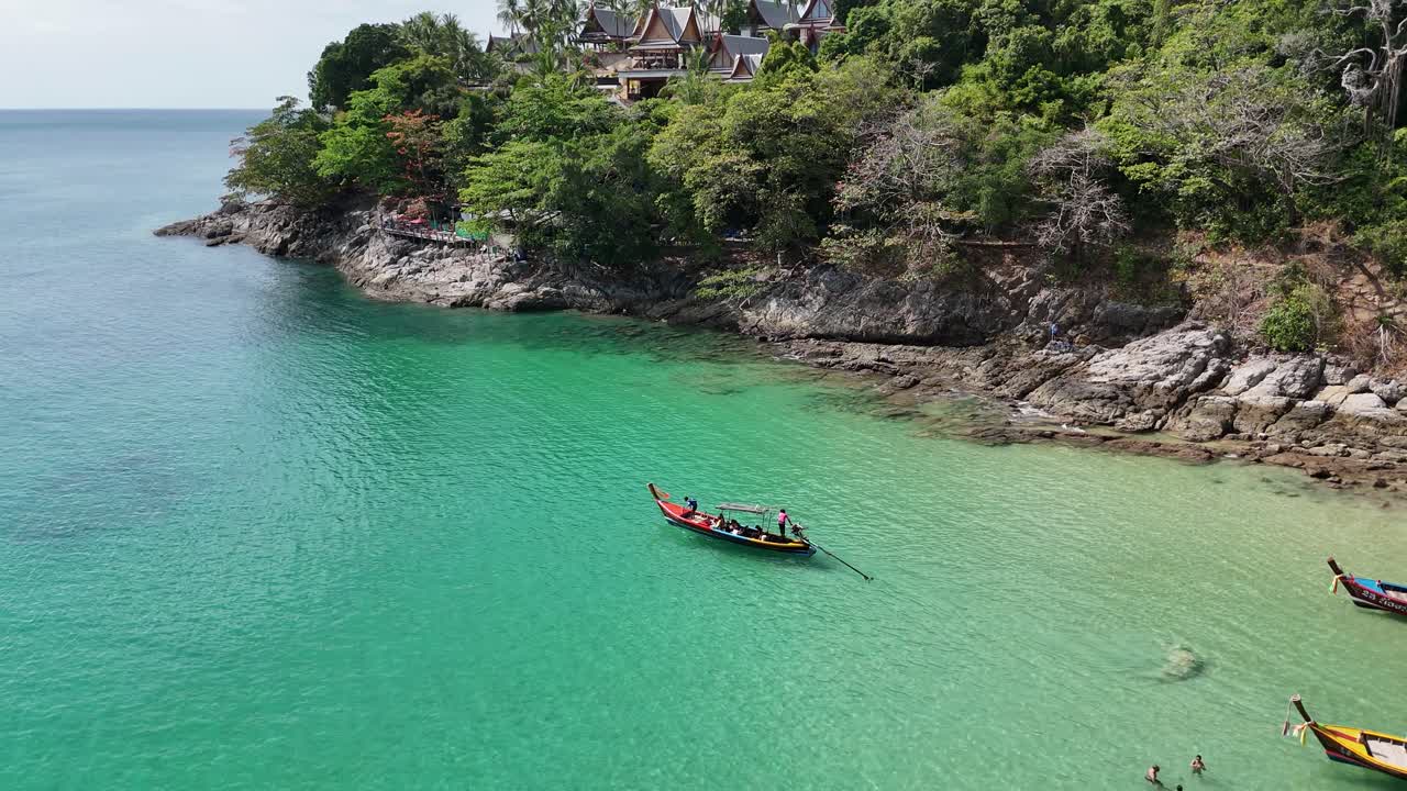 Riprese con drone catturano acque turchesi vivaci, barche longtail e una vegetazione lussureggiante lungo la pittoresca costa di Phuket in un sereno ambiente tropicale.