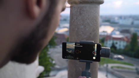 close up of man using smart phone and gimbal to film sunrise over city of budapest