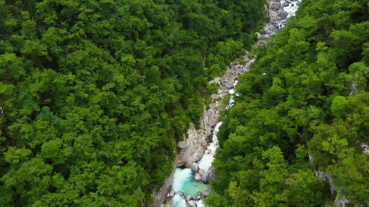 Ripresa aerea in tilt up di un ruscello del fiume Isonzo che scorre nella fitta foresta della Slovenia e della cascata di Boka sullo sfondo