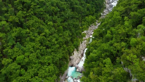 Toma-Aérea-Inclinada-Hacia-Arriba-De-La-Corriente-Del-Río-Soca-Que-Fluye-En-La-Silvicultura-Profunda-De-Eslovenia-Y-La-Cascada-Boka-En-El-Fondo