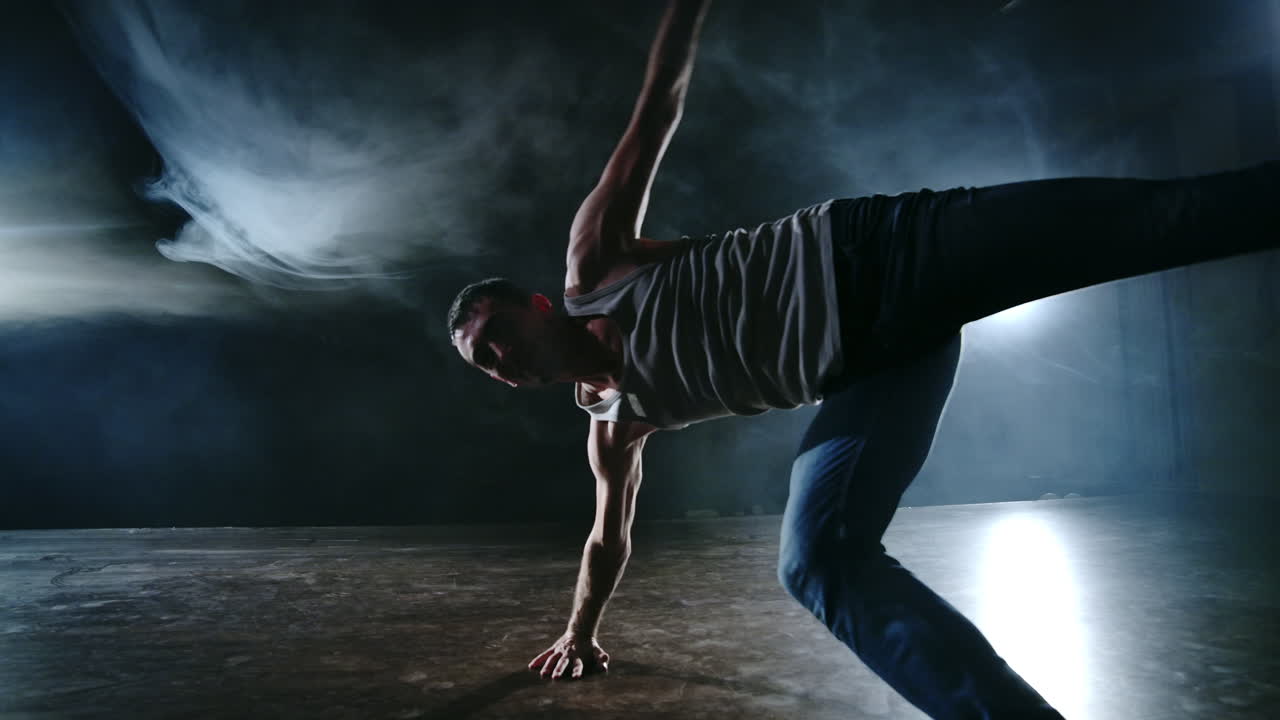 Male dancer performs a stunt jump with a rotation back and a revolution in the scene in the smoke in the spotlight. Modern ballet