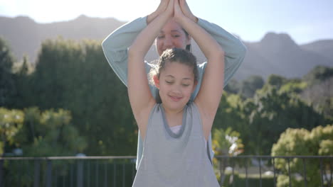 happy biracial mother and daughter practising yoga on terrace in sunny day, slow motion