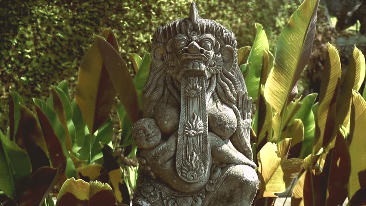 una hermosa escultura de piedra balinesa frente a grandes hojas verdes en un templo de ubud, bali - indonesia