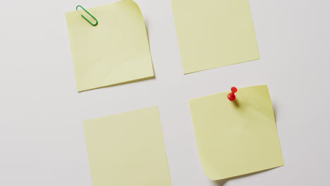 video of close up of four yellow memo notes with red pin and paper clip on white background