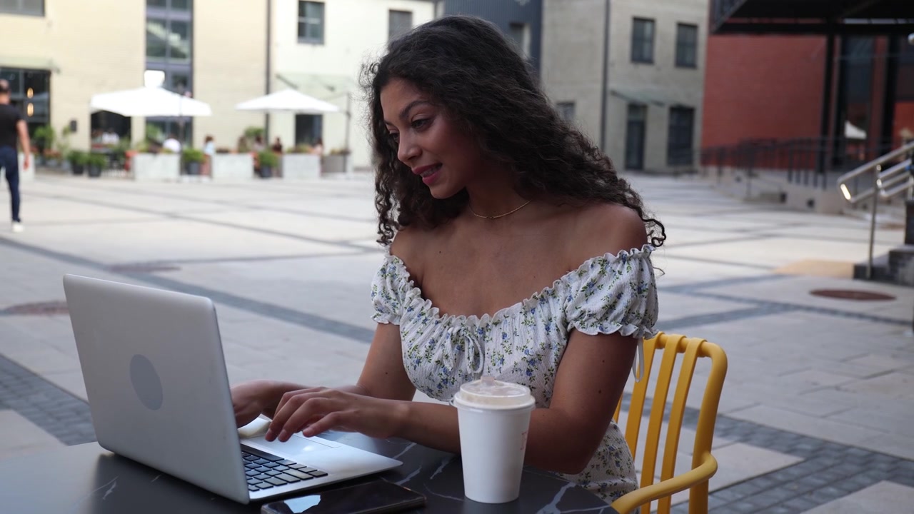 Donna sorridente che usa il laptop a un tavolo di un caffè all'aperto