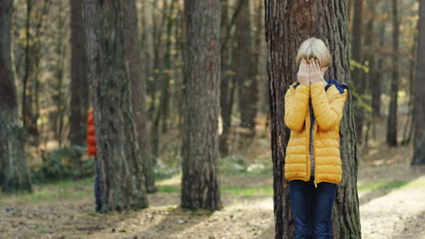 lindos niños caucásicos jugando al escondite en medio del bosque en un día soleado