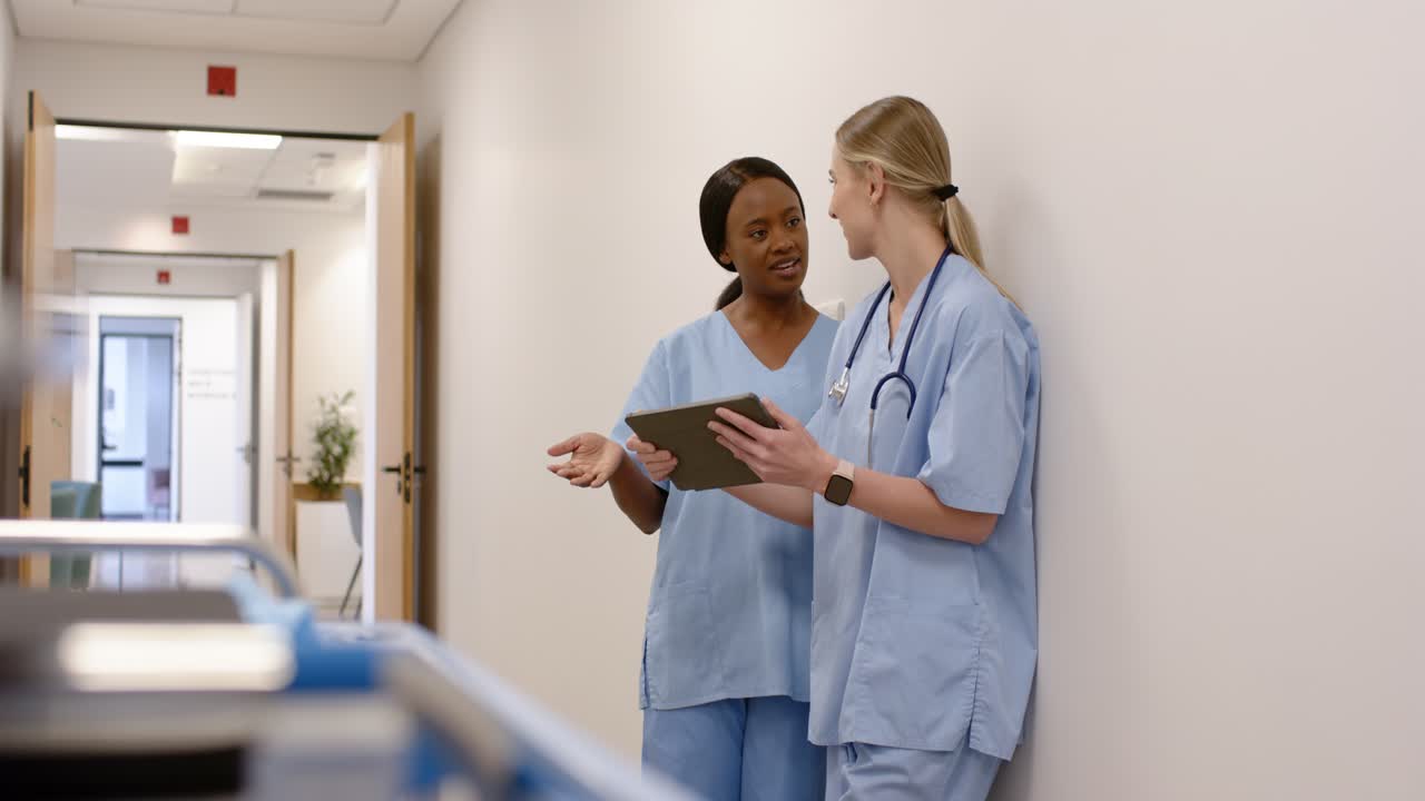 Diverse female nurses in hospital corridor after hand raise starting review, using tablet