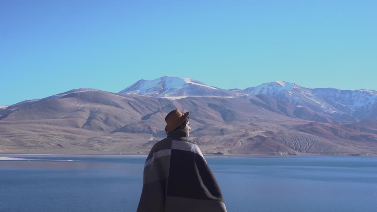 戴牛仔帽的当地男子在一个寒冷的晴朗早晨，在雄伟的山景中自由行走，背影
