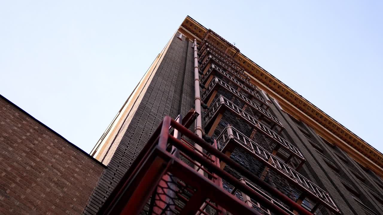 Slow pan down a classic historical industrial city building showcasing its beautiful red fire escape ladder system from the ground level floor. In 4k slow motion.