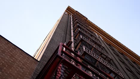 slow pan down a classic historical industrial city building showcasing its beautiful red fire escape ladder system from the ground level floor. in 4k slow motion.
