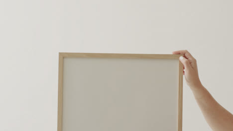manos de una mujer caucásica sosteniendo un marco con espacio de copia en fondo blanco contra una pared blanca