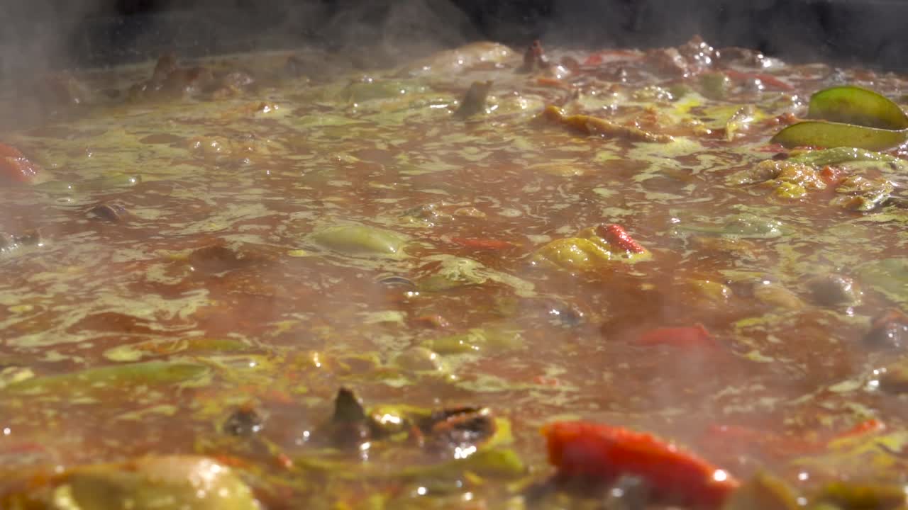 Un cuoco mescola una paella valenciana con la pala mentre il brodo bolle.
