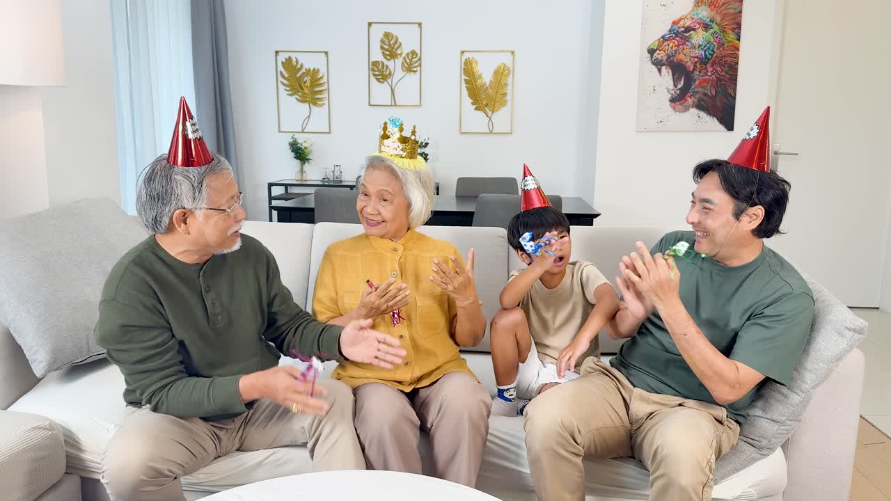 Three generations laugh and play with party hats in a brightly lit, modern living room