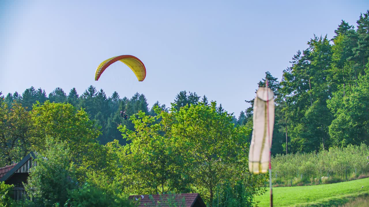 Tandem paragliders fly above green grass with flock of birds flying nearby, Padalci