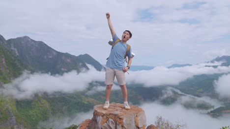 asian hiker male standing on the rock and raising his hand celebrating reaching up top of foggy mountain