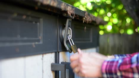 Beautifully-shot-close-up-of-a-padlock-and-latch-on-a-shed-with-hands-reaching-in-to-wrench-and-pull-at-the-lock-in-an-attemp-to-break-in,-with-stylish-bokeh