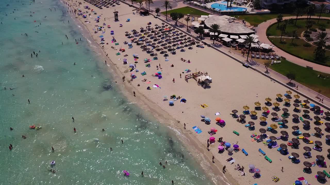 playa principal de cala con paraguas de colores y turistas nadando, vista aérea