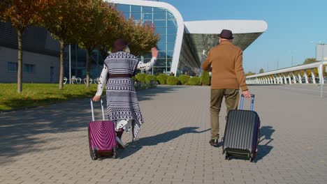 family grandmother grandfather walking with luggage suitcase bags to airport hall, celebrate dancing