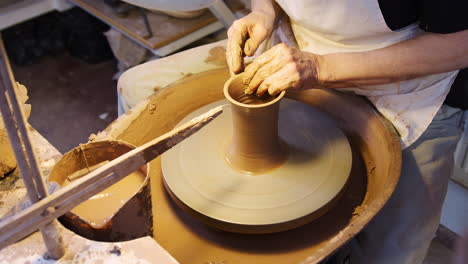 close up of male potter shaping clay for pot on pottery wheel in ceramics studio