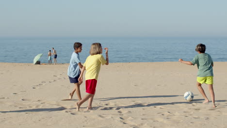 movimiento lento de niños felices jugando al fútbol en la playa de arena