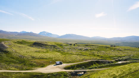 vehicle at the road amidst the green meadow and mountain range in rondane national park in norway