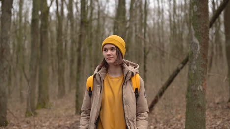 a young girl in a yellow woolen hat walks through the forest looking from side to side