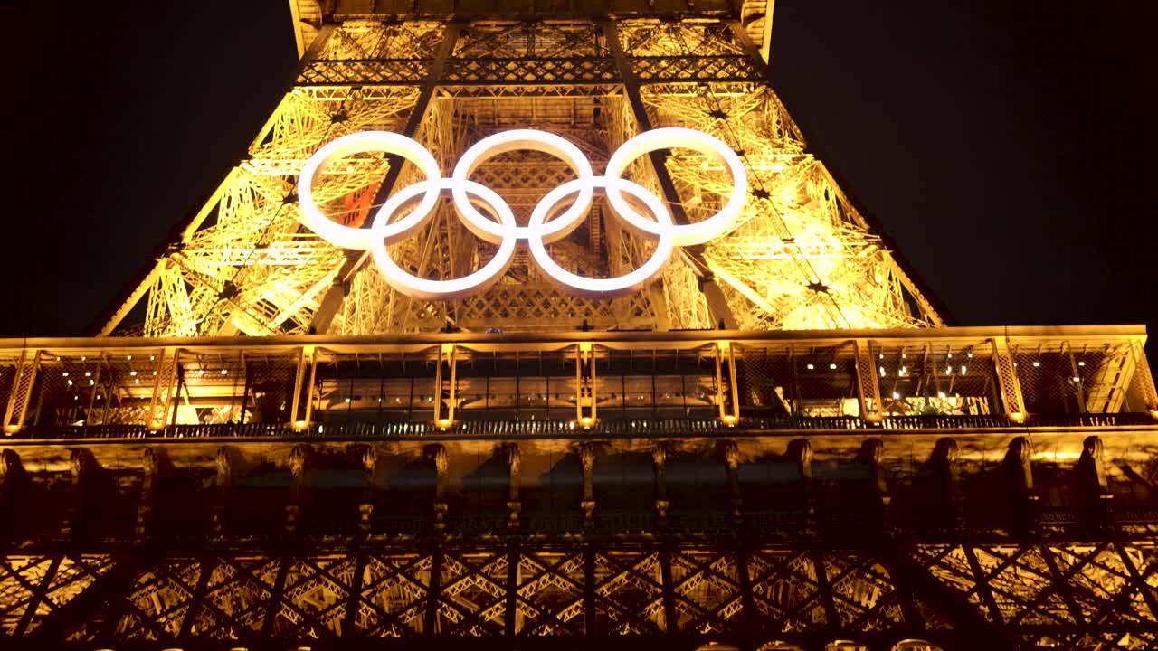 Eiffel Tower AT NIGHT 2024 Summer Olympics in Paris, France. Beautiful evening sunset, pretty night time sky, shows Olympic Rings symbol proudly shining bright. Historical Iconic Landmark 4K
