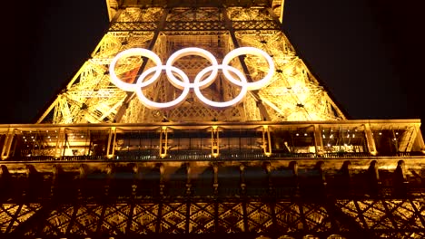 eiffel tower at night 2024 summer olympics in paris, france. beautiful evening sunset, pretty night time sky, shows olympic rings symbol proudly shining bright. historical iconic landmark 4k