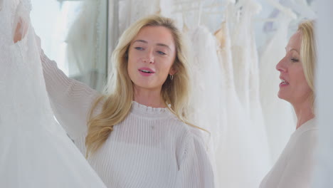 madre ayudando a su hija adulta a elegir el vestido de novia en la tienda de novias