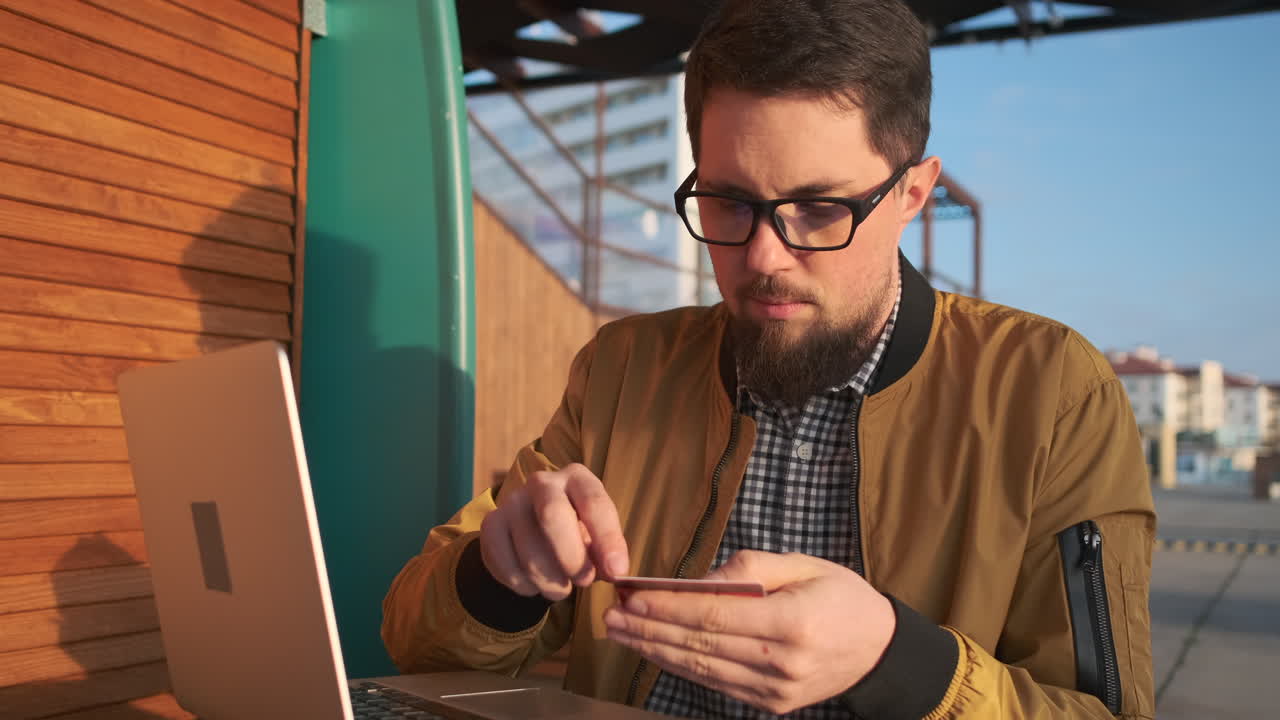 hombre pagando en línea con portátil y tarjeta de crédito afuera
