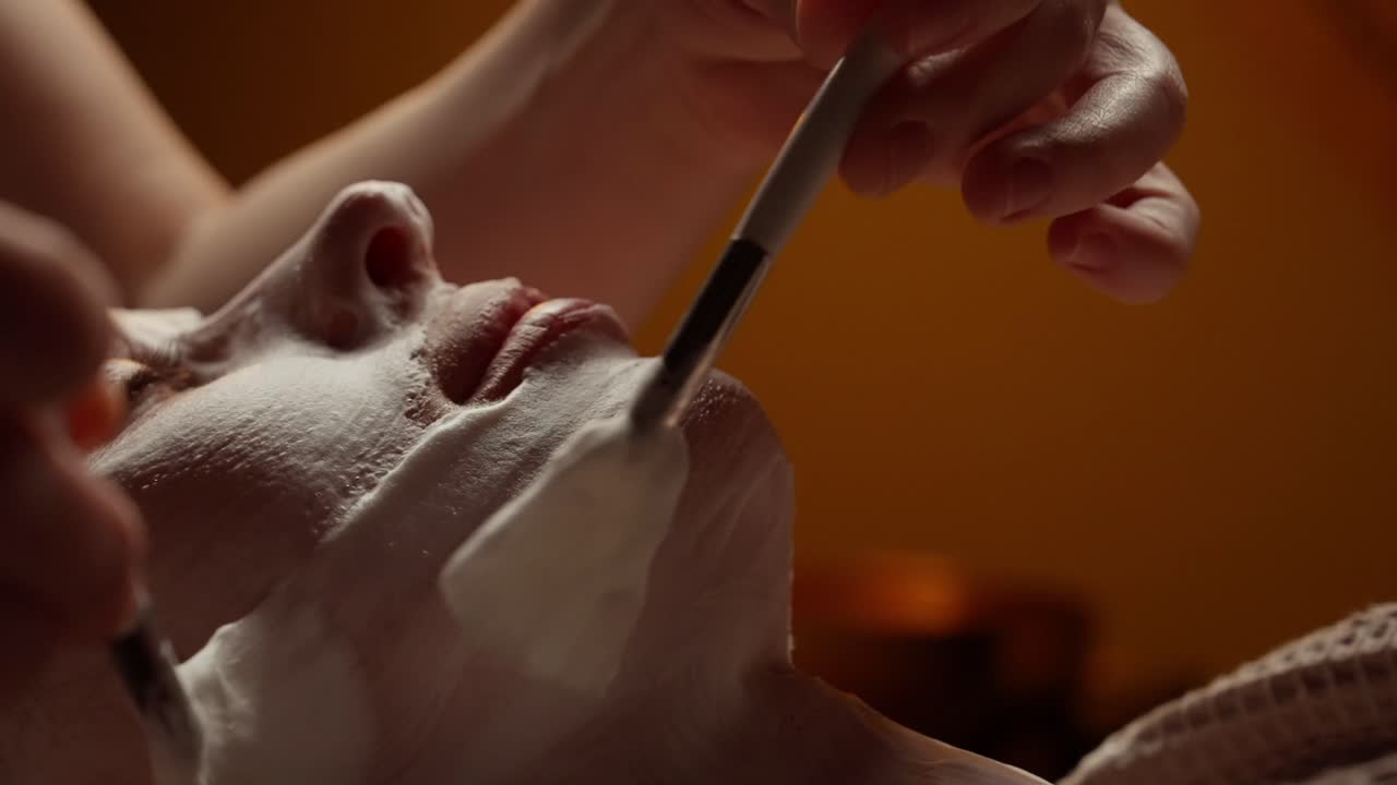 Schoonheidsspecialiste brengt gezichtsmasker aan op gezicht van vrouw in een spa