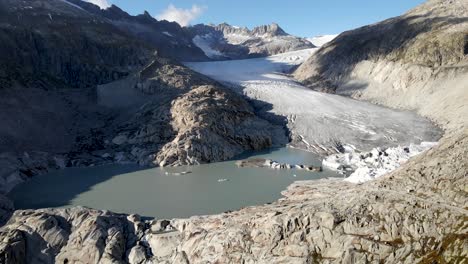 Aerial-flyover-from-Rhone-glacier-over-to-Furka-mountain-pass-at-the-border-of-Valais-and-Uri-in-Switzerland-with-a-view-of-the-road-and-closed-hotel