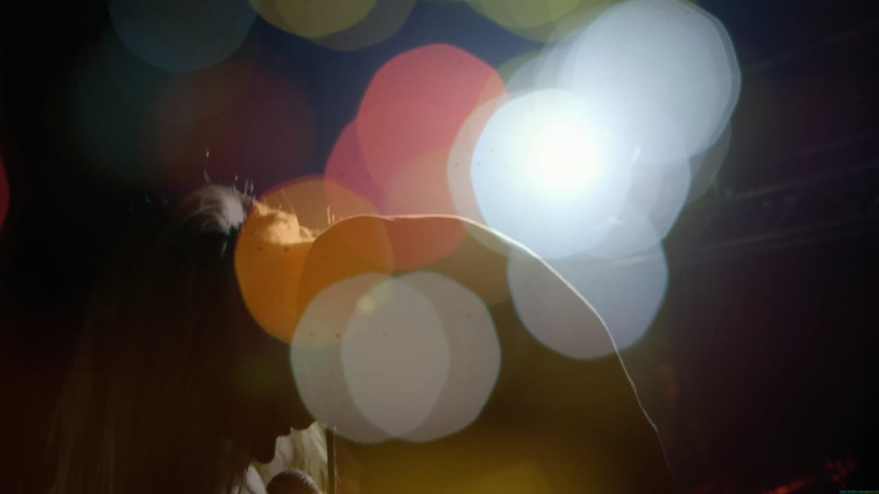 woman with long hair performing on music stage, with animated bokeh light flares