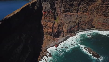 Una-Impresionante-Vista-Aérea-De-Una-Cadena-Montañosa-Que-Sobresale-Del-Océano,-Con-Olas-Rompiendo-Contra-Los-Escarpados-Acantilados