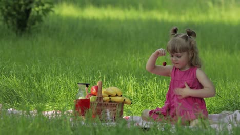 weekend at picnic. lovely caucasian child girl on green grass meadow eating merry, cherry