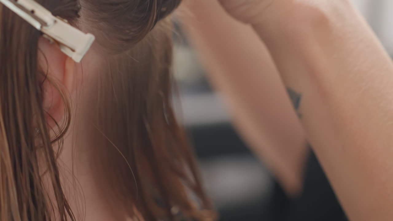 Primer plano de unas manos creando pequeñas trenzas sección por sección, un estilista sujetando el pelo con una pinza y controlando la tensión, formando una textura bohemia, escena entre bastidores en un salón con un cliente sentado y una técnica cuidadosa