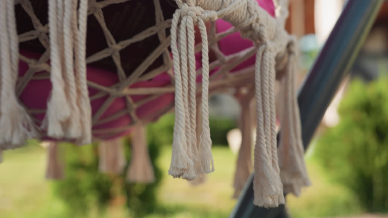 Bright Decorative Fringes, Vibrant Boho Tassels Complement Tranquil Garden Setting, Sunlit Tassels Hanging On Bohemian Swing Enhance Serene Porch Atmosphere Surrounded By Garden Foliage